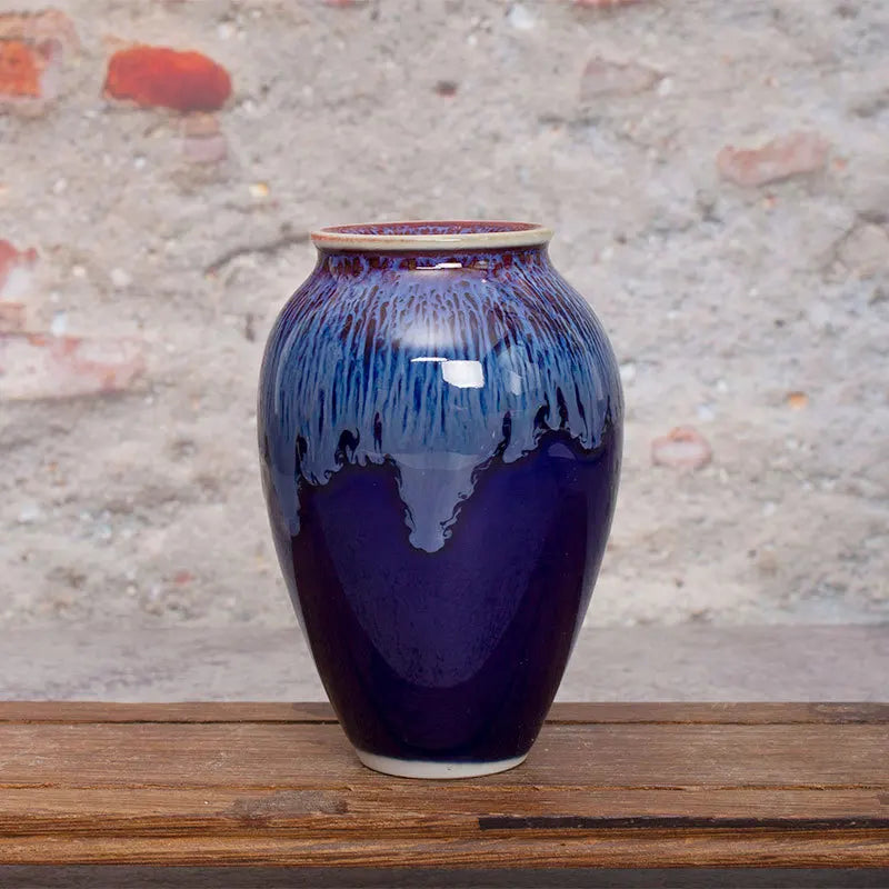 Magnifique vase en céramique orné de reflets bleu foncé et violet, posé sur une surface en bois.