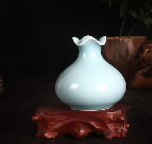 Un vase en céramique bleu pâle avec des détails sculptés, posé sur un support en bois foncé.