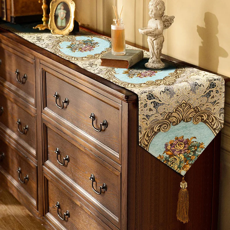 Un meuble en bois ancien avec des tiroirs, recouvert d'un chemin de table décoratif et orné d'objets de décoration vintage, créant une ambiance chaleureuse et élégante.