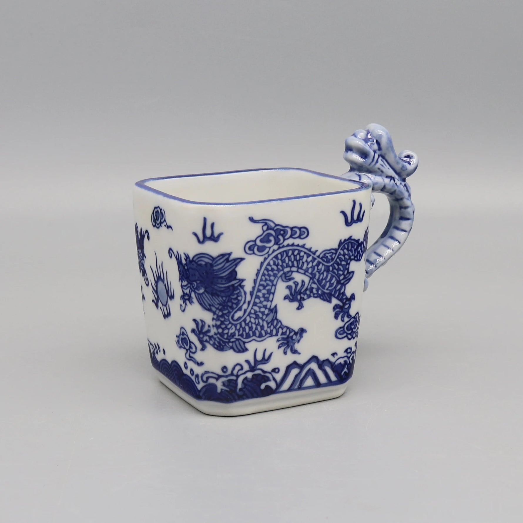 Cette tasse en porcelaine blanche et bleue est décorée d'un motif de dragon stylisé, offrant une touche d'exotisme oriental.
