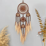 Suspension murale en forme de capteur de rêves, ornée de motifs géométriques et de pompons en fibres naturelles, suspendu dans un décor végétal.
