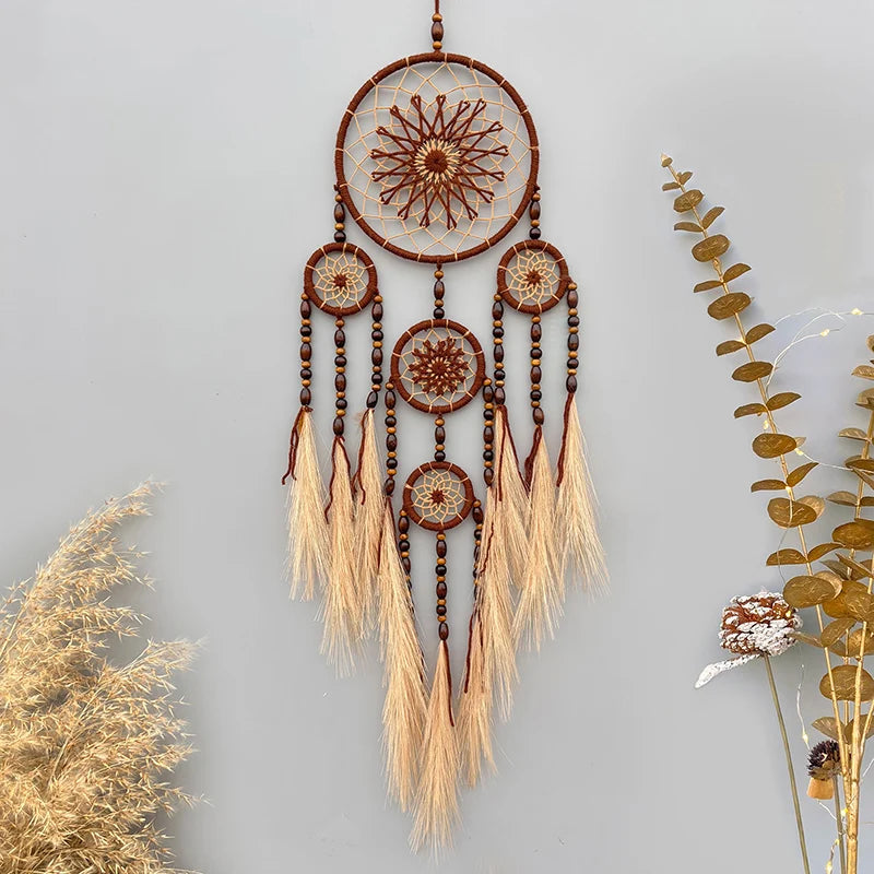 Suspension murale en forme de capteur de rêves, ornée de motifs géométriques et de pompons en fibres naturelles, suspendu dans un décor végétal.