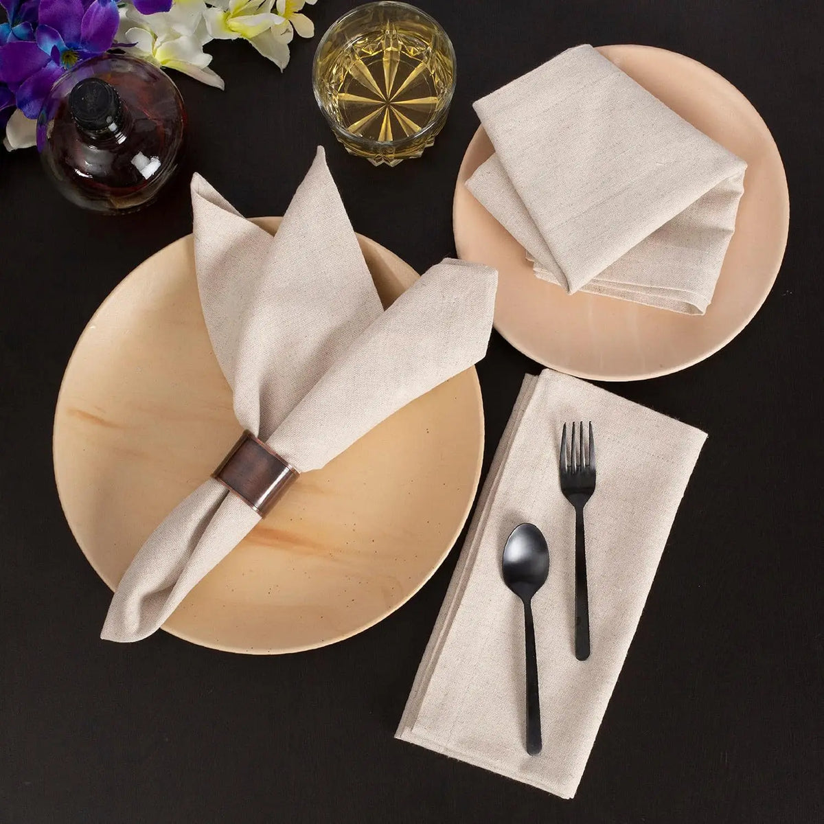 Une image élégante d'une table dressée avec une assiette, des serviettes en lin, des couverts et un verre de whisky, entourée de fleurs colorées.