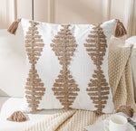 Coussin blanc orné de motifs géométriques texturés en beige, sur fond de couverture en tricot et d'une tasse blanche posées sur un plan de travail clair.