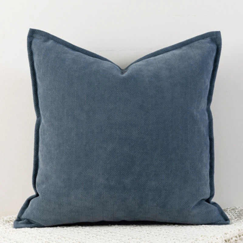 Coussin décoratif gris en velours avec un motif en chevrons, posé sur un sol clair.