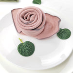 Un foulard rose enroulé en spirale, entouré de feuilles vertes, sur un plat blanc.