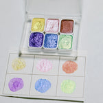 peintures aquarelle palette compacte bleu vert violet rose beige jaune blanc texture granuleuse opaques