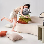 Une jeune femme assise sur un canapé beige, entourée de coussins colorés.