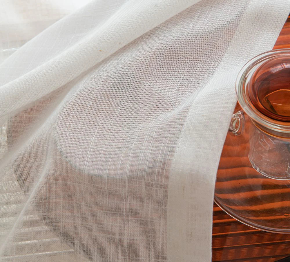 Détail de la texture du tissu blanc du voilage posé sur une carafe en verre.