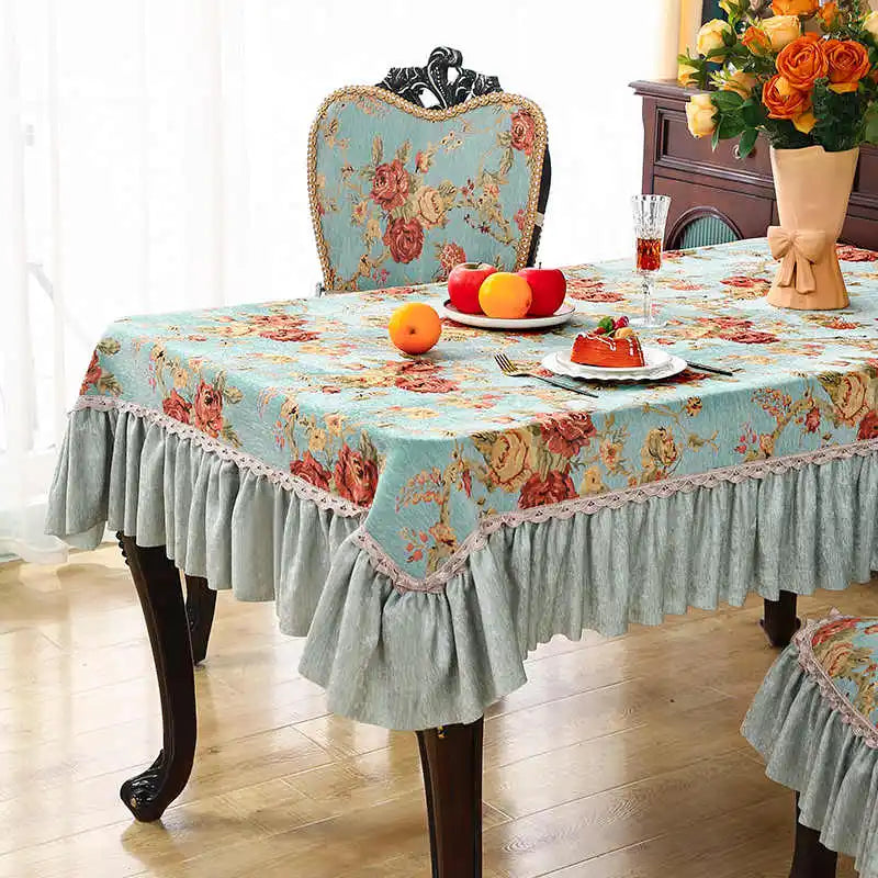 Cette image représente une table élégante avec une nappe florale de couleur turquoise, ornée de décorations et d'assiettes de dessert. Un bouquet de roses orange et jaune complète cette scène de salle à manger accueillante.