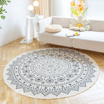 Un tapis rond et décoratif avec un motif de cercles concentriques dans des tons de gris, placé sur un parquet clair dans un salon lumineux et bien aménagé.