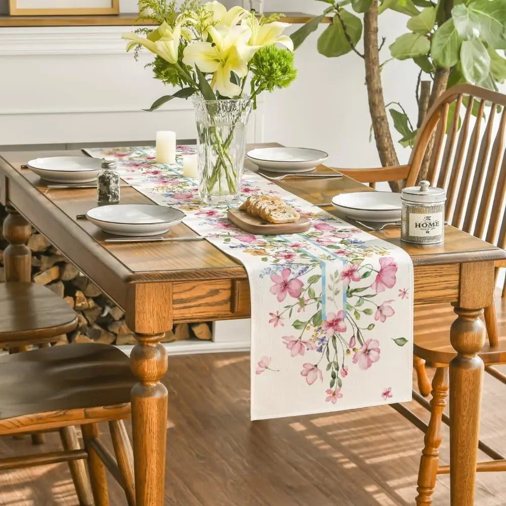 Une table de cuisine en bois décorée d'un bouquet de fleurs jaunes et d'un chemin de table à motifs floraux, avec de la vaisselle et des accessoires pour une atmosphère chaleureuse et accueillante.
