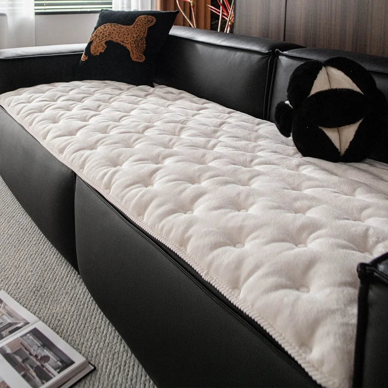 Un canapé en cuir noir recouvert d'un épais couvre-lit douillet beige et parsemé d'oreillers décoratifs, offrant un espace confortable et douillet.