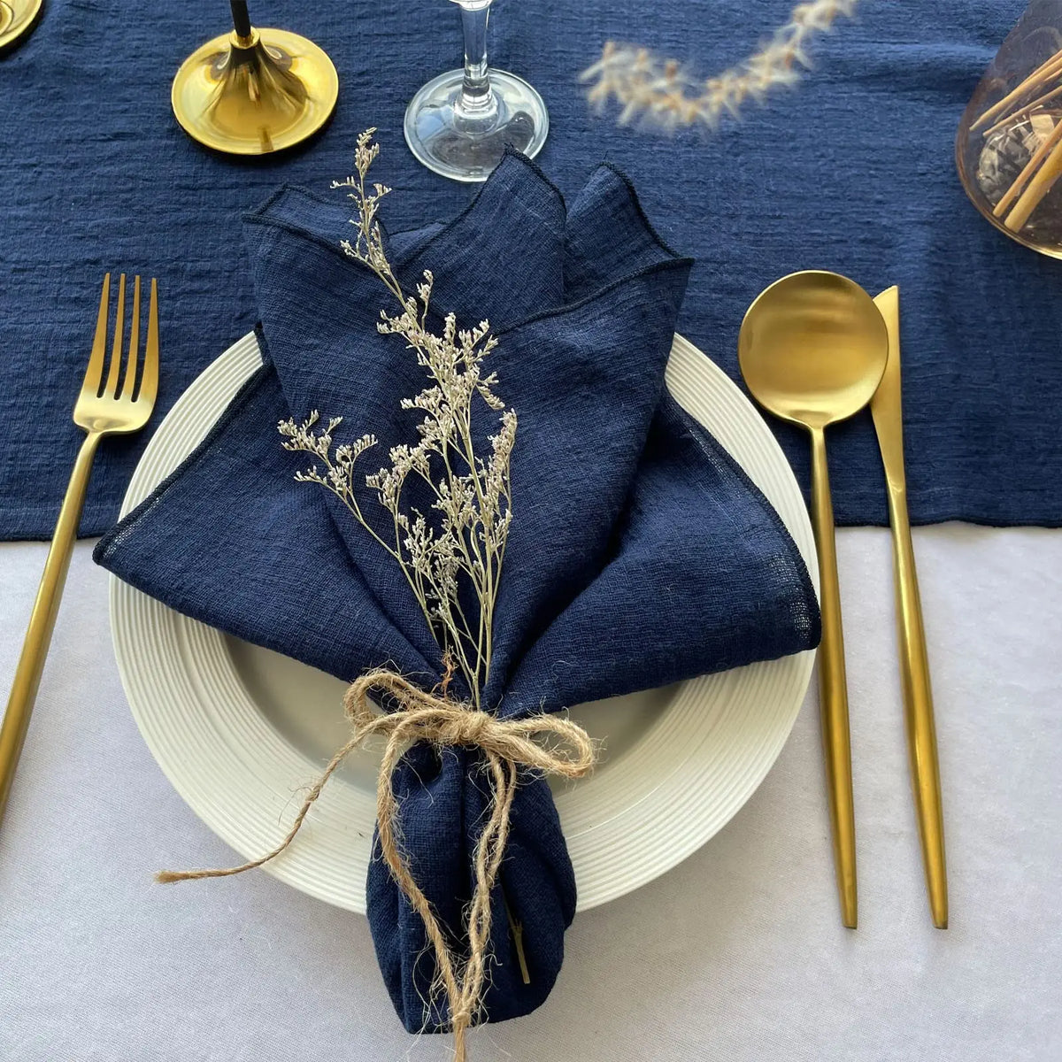 Élégante table de fête avec couverts dorés, serviette en lin bleu foncé et fleurs séchées, sur un fond bleu nuit.