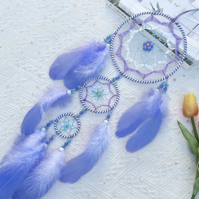 Un capteur de rêves décoratif aux tons bleutés, agrémenté de plumes, de motifs géométriques et de perles, disposé sur un fond blanc texturé.