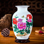 Ce vase en porcelaine peinte à la main présente de belles fleurs de pivoine rouges et roses, ainsi qu'un papillon, sur un fond blanc.