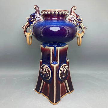 Un vase décoratif en céramique de style antique avec des motifs floraux et des ornements en relief, dans des tons de bleu et de brun, évoquant une ambiance élégante et sophistiquée.