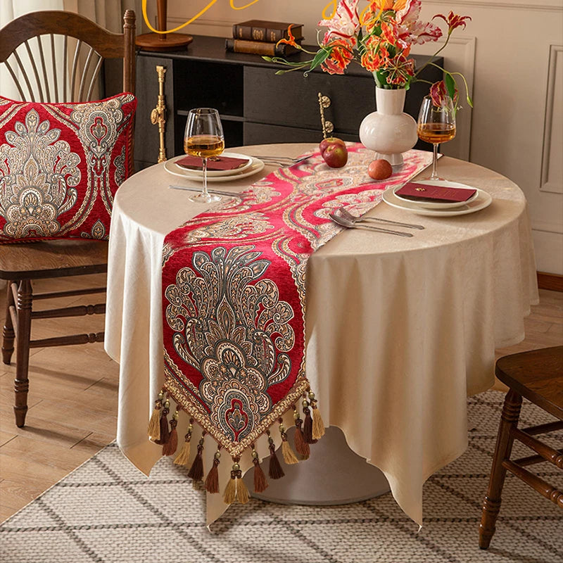 Une table ronde richement décorée avec un chemin de table rouge et doré, des assiettes, des verres et des fleurs, créant une ambiance chaleureuse et élégante.