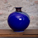 Un vase en céramique d'un bleu intense, posé sur une surface en bois rustique, reflétant la lumière de manière élégante.