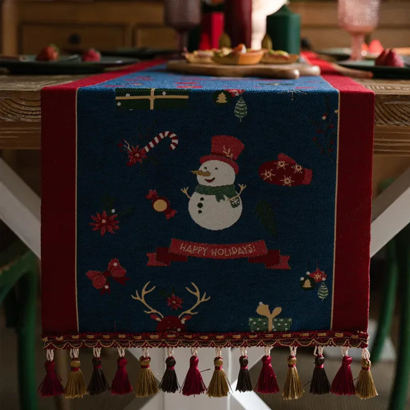 Une nappe de table décorée d'un bonhomme de neige souriant et d'ornements de Noël sur un fond bleu profond, invitant à la joie et à la célébration des fêtes.
