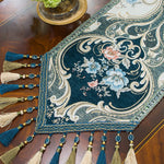Ce magnifique chemin de table en velours présente un motif floral élégant aux couleurs profondes et chatoyantes, rehaussé de pompons et de perles qui ajoutent une belle touche de sophistication.