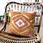 Coussin orné de motifs géométriques colorés, posé sur un fauteuil en osier.