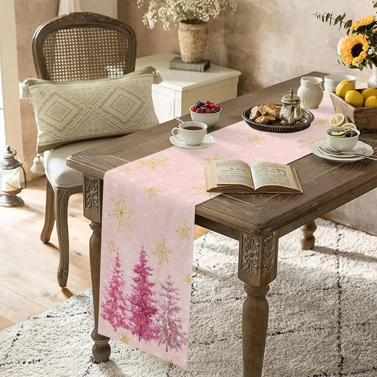 Une table en bois rustique avec une nappe rose ornée de motifs d'arbres, accompagnée d'une chaise en cannage, d'un vase de fleurs et d'un livre ouvert, créant une atmosphère chaleureuse et accueillante.