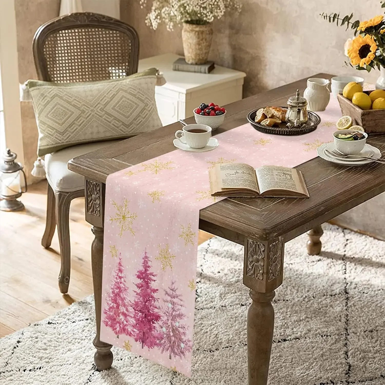 Une table en bois rustique avec une nappe rose ornée de motifs d'arbres, accompagnée d'une chaise en cannage, d'un vase de fleurs et d'un livre ouvert, créant une atmosphère chaleureuse et accueillante.