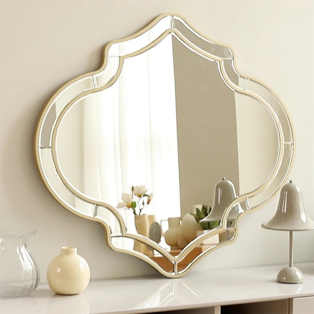 Miroir décoratif mural de forme élégante avec un cadre doré et des ornements, placé sur une console blanche avec des accessoires de décoration.