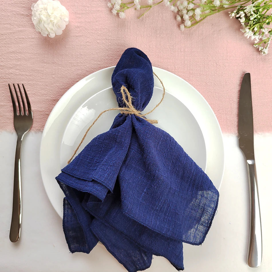 Une assiette élégante avec une serviette en lin bleu marine nouée avec de la ficelle, entourée de fleurs blanches et d'ustensiles de table.
