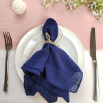 Une assiette élégante avec une serviette en lin bleu marine nouée avec de la ficelle, entourée de fleurs blanches et d'ustensiles de table.