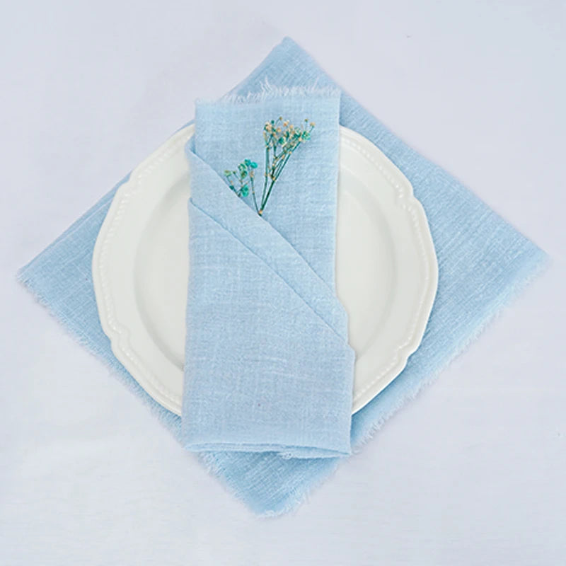 Une serviette bleue pliée avec une fleur brodée sur la table blanche.