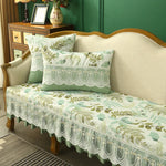 Un canapé vintage élégant avec des motifs floraux et des détails en dentelle blanche sur un fond vert tendre, créant une ambiance chaleureuse et naturelle.