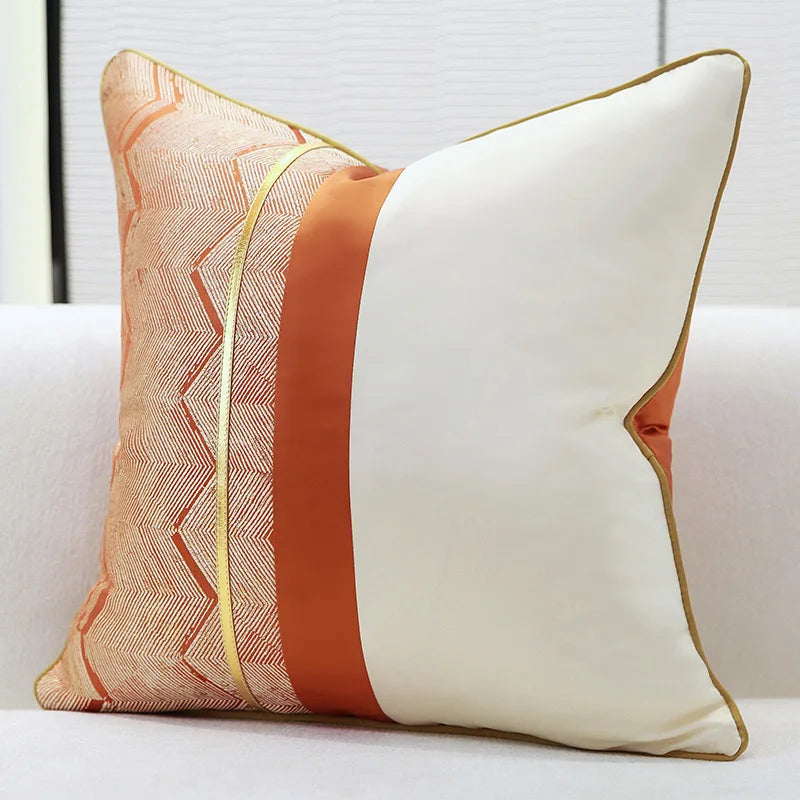Coussin décoratif beige et orange avec motifs géométriques et bordure dorée.