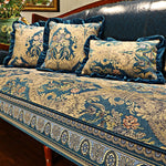 Ce canapé rembourré présente un motif floral doré et ornemental sur un fond bleu foncé, avec des coussins assortis, offrant un style élégant et sophistiqué dans un intérieur chaleureux.