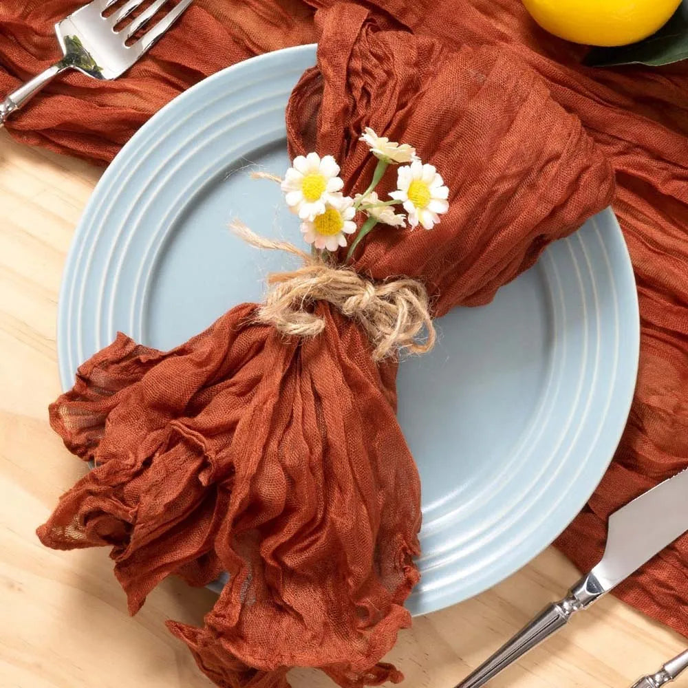 Une assiette décorative avec un linge de table rougeâtre et de jolies fleurs de camomille pour une ambiance chaleureuse et rustique.