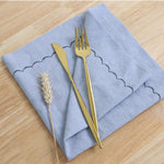 Une nappe grise élégante avec une fourchette et un couteau dorés posés sur le côté, accompagnés d'un épi de blé, créant une belle composition sur un fond en bois clair.
