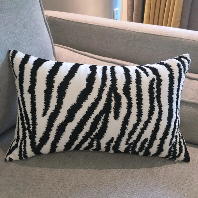 Coussin décoratif au motif zébré noir et blanc, placé sur un canapé gris, dans un intérieur cosy.