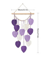 Suspension décorative murale en macramé avec des feuilles violettes et blanches, de forme géométrique, suspendue à une tige en bois.