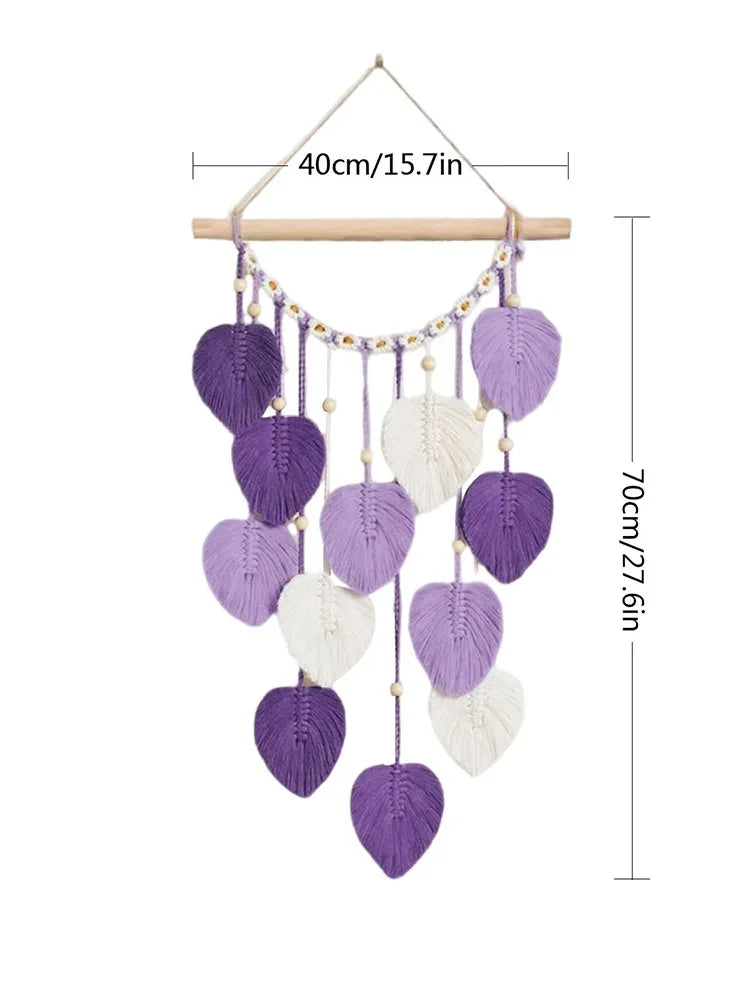 Suspension décorative murale en macramé avec des feuilles violettes et blanches, de forme géométrique, suspendue à une tige en bois.