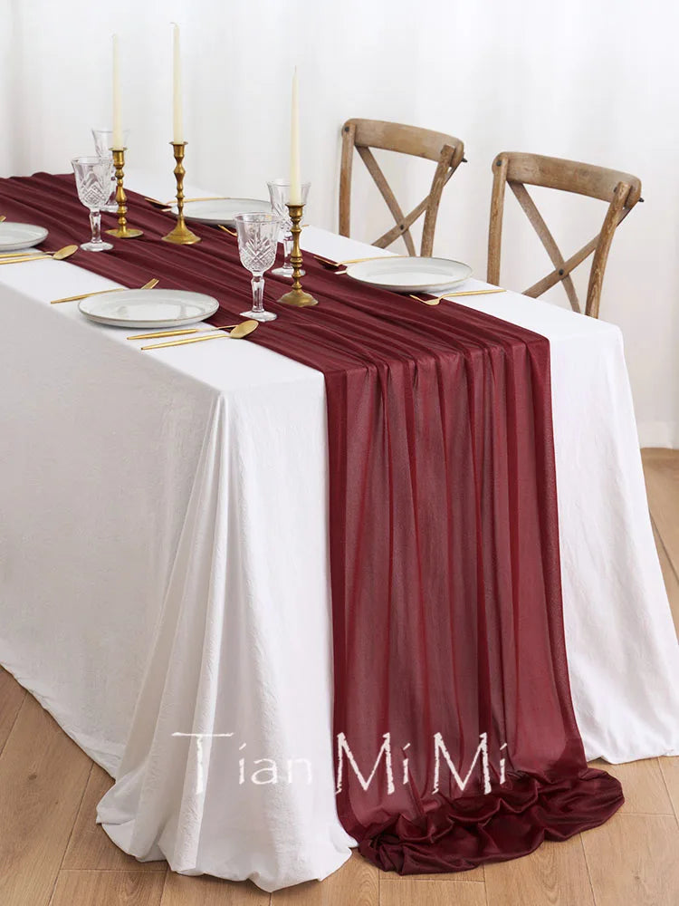 Table de fête élégante avec nappes blanches, chemin de table et accessoires décoratifs de couleur bordeaux.