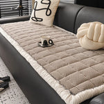 Tapis moelleux en fibres naturelles avec motif tressé, coussin décoratif et bougie sur un canapé en cuir noir, créant une atmosphère cocooning et confortable.