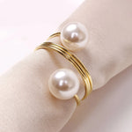 Une élégante bague en or sertie de deux perles blanches posée sur un tissu beige.