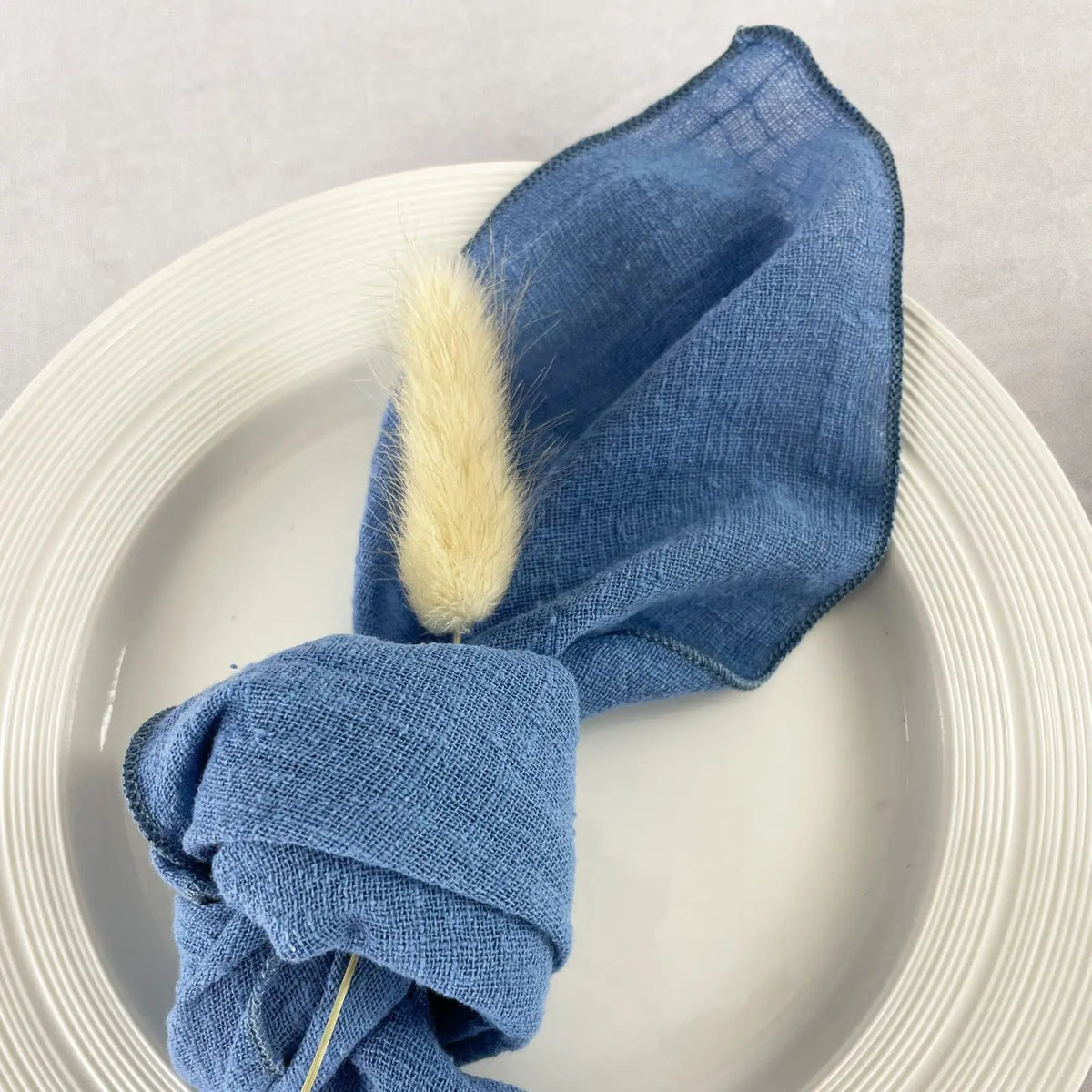 Serviette grise enroulée sur un plat blanc, ornée d'une touffe de fourrure beige.