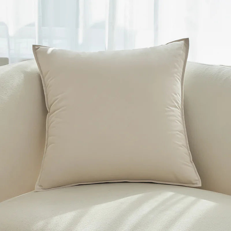 Un coussin beige confortable et douillet, posé sur un canapé blanc, dans une pièce avec de grandes fenêtres.