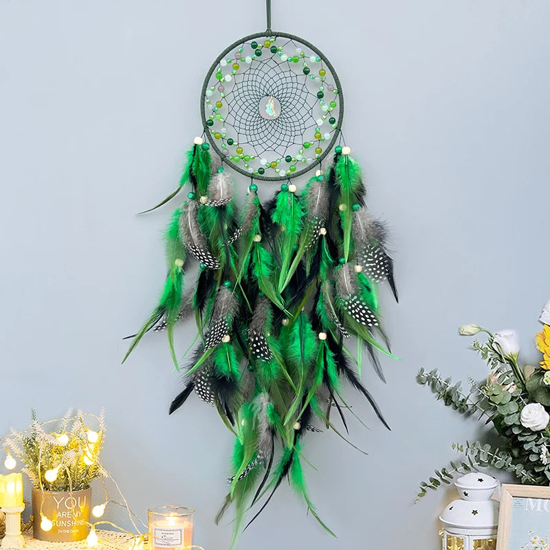 Un magnifique attrape-rêves vert orné de plumes et de perles, suspendu devant un arrière-plan clair, avec des fleurs et des bougies décoratives à proximité.