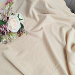Cette image représente un bouquet de fleurs multicolores, notamment des roses délicates, posé sur une surface en velours beige.