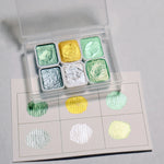 peintures aquarelle palette compacte bleu vert violet rose beige jaune blanc texture granuleuse opaques