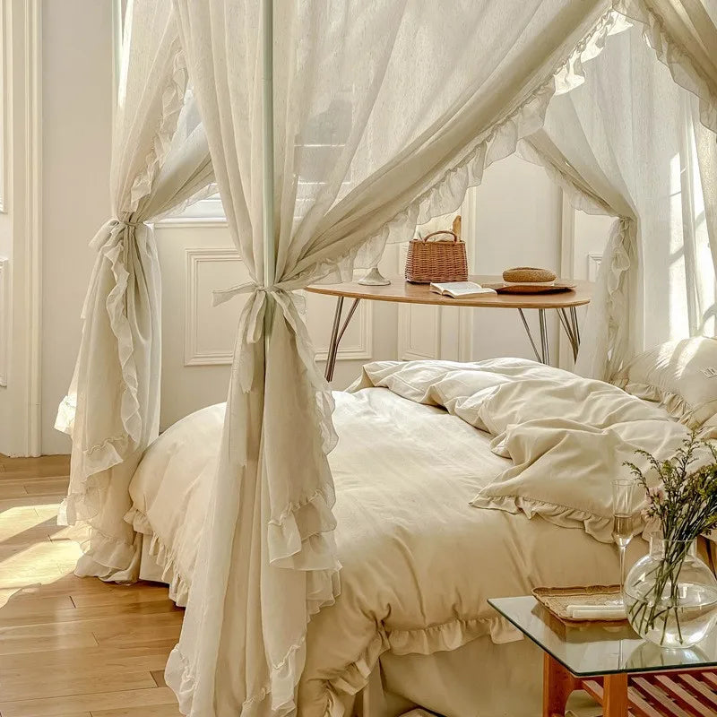 Chambre de style romantique avec des rideaux blancs délicats et une literie froissée, une petite table en bois au-dessus du lit et un panier en osier posé sur la table.