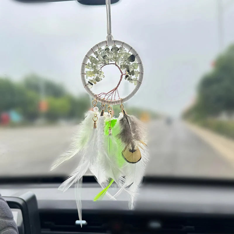 Un pendentif onirique en forme d'arbre de vie orné de perles vertes et de plumes translucides, accroché au rétroviseur d'un véhicule.